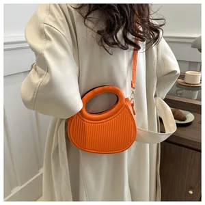 Close-up of bright orange pleated crossbody bag with a curved handle on a model