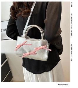 Detail of silver crossbody bag featuring pink silk bows on a model with striped shirt