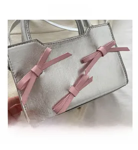 Close-up of silver patent leather handbag featuring cute pink bow decorations