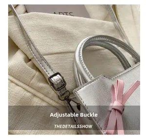 Detail of adjustable metal buckle on silver crossbody bag with a pink bow decoration