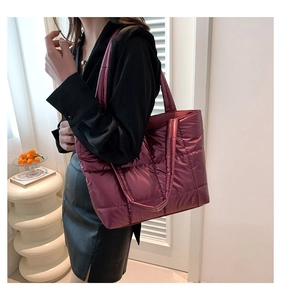 Model wearing a large burgundy quilted puffer tote bag in glossy nylon material