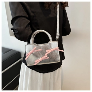 Détail du sac argenté métallisé avec trois nœuds roses et poignée ronde en métal