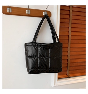 Détail d'un sac cabas matelassé noir suspendu à un porte-manteau en bois dans une pièce
