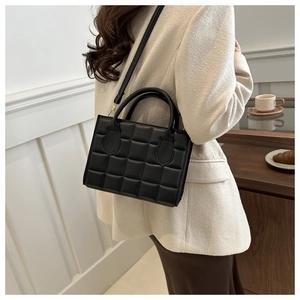 Detail of a black quilted crossbody bag with gold hardware shown in a lifestyle setting