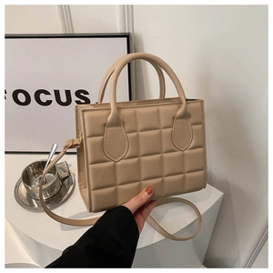Close-up of beige quilted handbag showing square stitching and adjustable shoulder strap