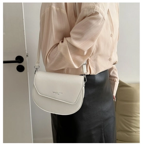 Détail du sac selle blanc montrant la texture du cuir et l'inscription dorée Fashion Trend