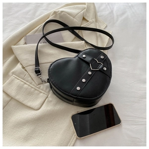 Détail d'un sac à main noir en forme de cœur avec clous argentés sur un blazer crème