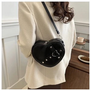 Modèle portant un sac bandoulière noir en forme de cœur avec rivets dans un café cosy