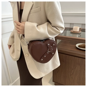 Détail d'un sac à bandoulière en forme de cœur marron foncé avec rivets argentés et boucle métal