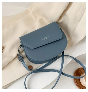 Détail du sac selle bleu mat avec logo doré et finitions métalliques foncées