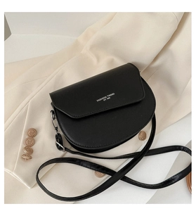 Détail du sac selle en cuir noir avec lettrage blanc sur un blazer beige clair