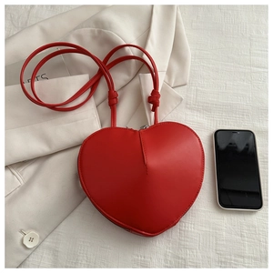 Détail du sac bandoulière rouge en forme de cœur sur blazer beige avec smartphone de référence