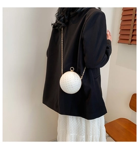 Detail of a white sphere pearl clutch bag with gold chain strap on a model shoulder