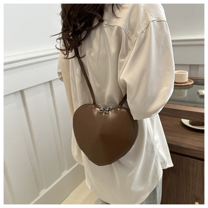 Détail d'un sac bandoulière en cuir marron foncé en forme de cœur porté à l'épaule