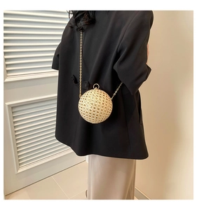 Detailed view of spherical evening bag with woven texture and gold chain on black blazer