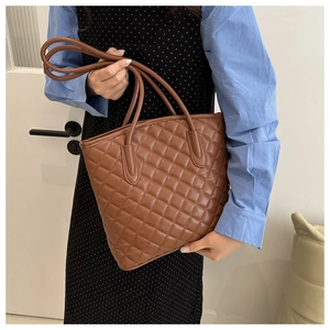Brown quilted tote bag with diamond pattern stitching and slim shoulder straps on a model