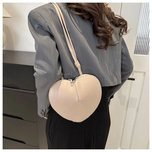 Sac bandoulière chic en forme de cœur crème porté sur un blazer gris élégant