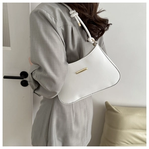 Close-up of white leather underarm bag featuring a knotted strap and gold metal bar