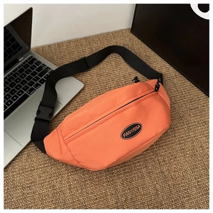 Dettaglio di una borsa a tracolla arancione in nylon oxford con logo su un tappeto di paglia