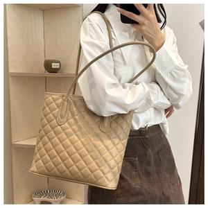 Model wearing a large beige quilted tote bag with diamond stitching and slim shoulder straps
