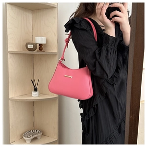 Detailed close-up of a pink leather underarm bag featuring a gold metal bar and knotted strap