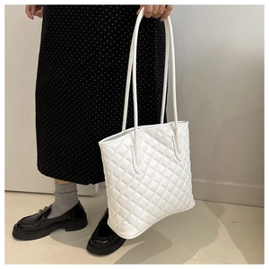 Detailed view of white quilted tote bag with diamond stitching and slim shoulder straps