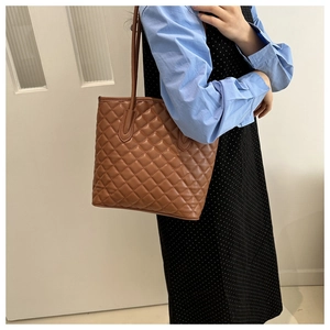 Brown quilted tote bag with diamond stitching shown on shoulder of a model in a dress