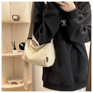 Detail of beige corduroy half-moon bag with wide strap and black plush charm