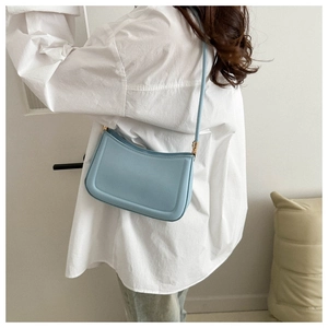 Gros plan d'un sac à bandoulière minimaliste en cuir bleu clair avec coutures et détails dorés