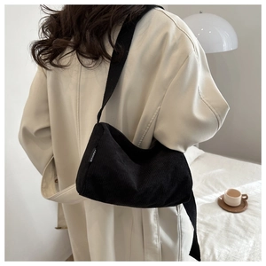 Detail of black corduroy tote bag showing the white fashion label and soft ribbed texture