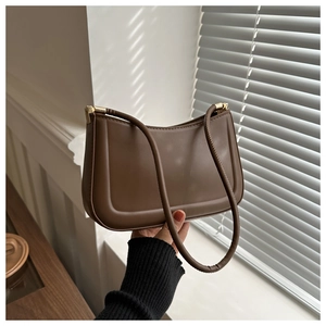 Minimalist dark brown leather shoulder bag with sleek gold hardware in a sunlit setting