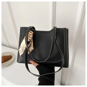 Detail of a black tote bag with white contrast stitching and a floral silk scarf handle