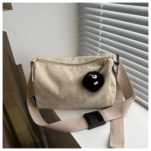 Detail of beige corduroy tote bag showing wide shoulder strap and black plush pendant