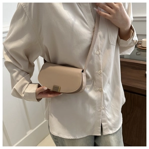 Close-up of minimalist beige saddle bag worn by a model in a modern interior setting