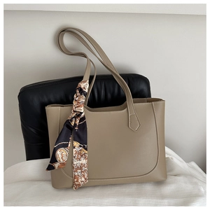 Detail of khaki tote bag with a decorative silk scarf tied to the leather handle