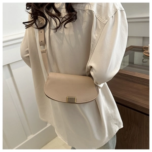 Detail of minimalist beige saddle bag with gold buckle on a model in home setting