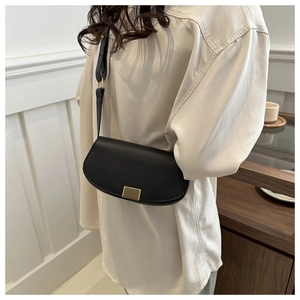 Close-up of black PU leather saddle bag with gold metal clasp on model's shoulder