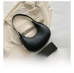 Top view of black crescent hobo bag with smartphone for size comparison on beige fabric