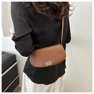 Caramel brown leather saddle bag with gold textured clasp worn by model in home setting