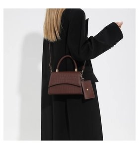 Detail of dark brown crocodile embossed tote bag with braided handle and mini pouch charm