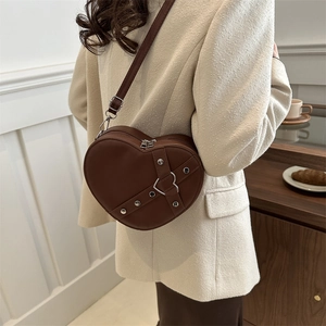 Sac bandoulière marron en forme de cœur avec clous argentés porté par un mannequin