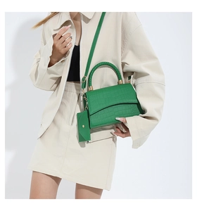 Detail of green crocodile-patterned handbag with woven handle and matching mini purse
