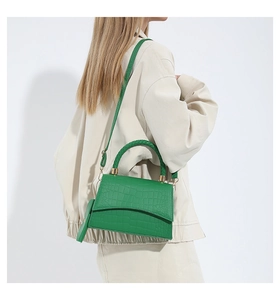 Detail of green crocodile texture handbag with woven handle and gold hardware