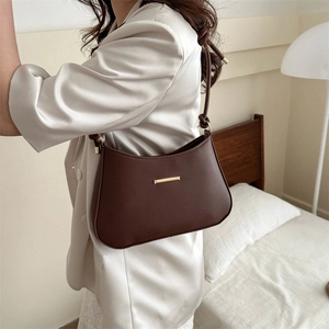 Minimalist dark brown half-moon underarm bag with gold metal bar in a cozy bedroom scene