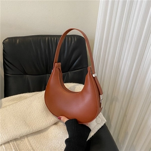 Minimalist caramel brown crescent underarm bag with silver hardware on leather chair