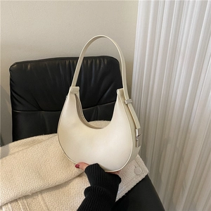 Minimalist off-white crescent leather underarm bag with silver buckle on a textured chair