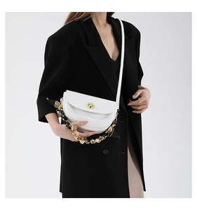 White saddle bag with gold clasp and resin chain strap worn over a black blazer