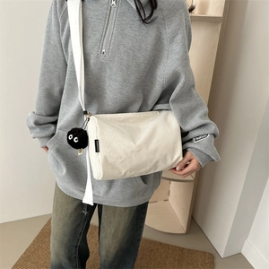 White corduroy tote bag with wide strap and black plush charm accessory on gray sweatshirt