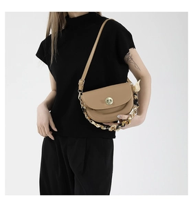 Detail of khaki saddle bag with gold lock, chain, and floral scarf accent on model