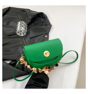 Close-up of green saddle bag with gold clasp and silk scarf wrapped chain handle